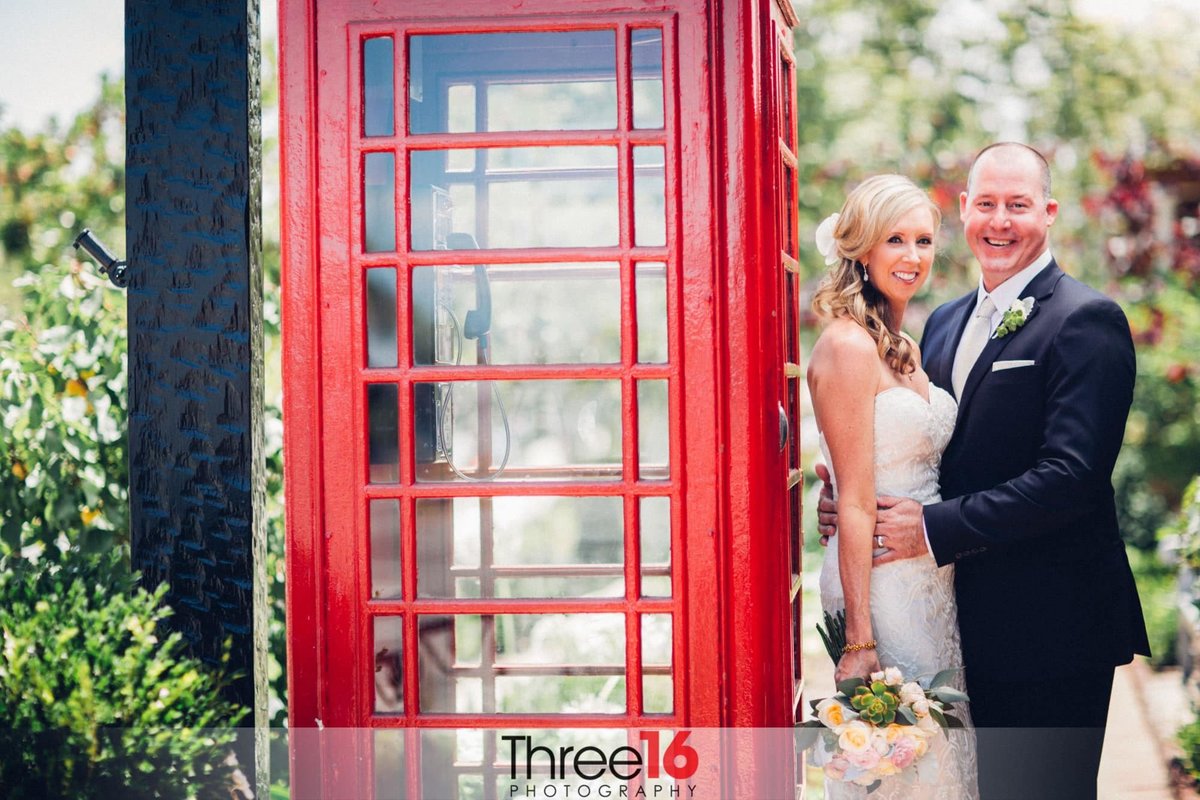 Newly married couple embrace as they pose for photos next to phone booth