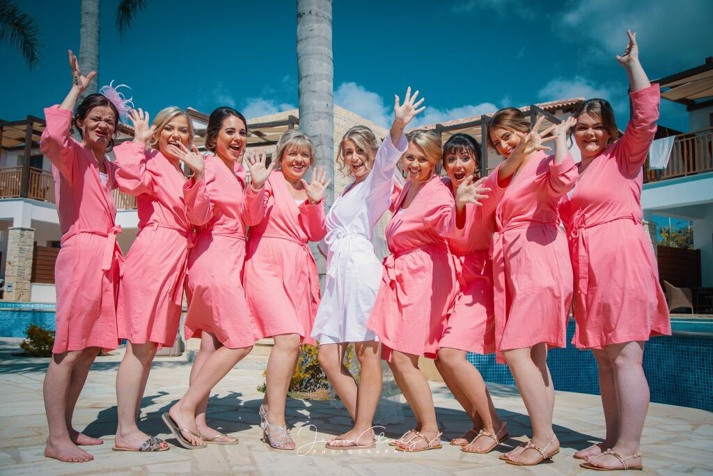 Bride dressed in white robe surrounded by her bridal party wearing matching coral robes