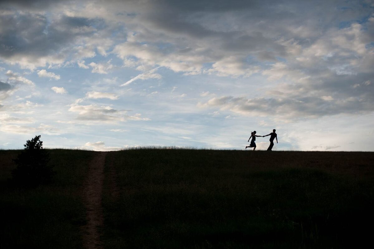 a silhouette on a tall hill with pretty clouds of a man pulling a woman along behind