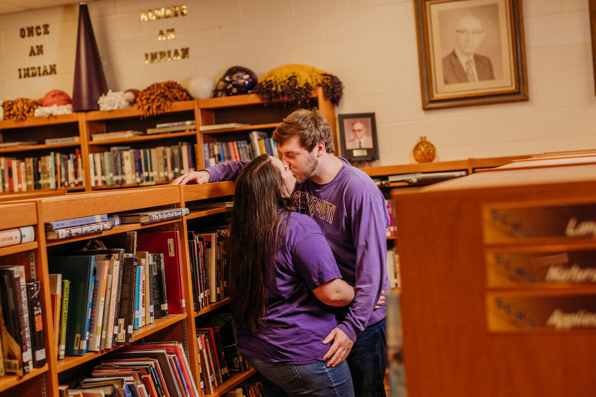 photo of man and woman kissing between bookshelves