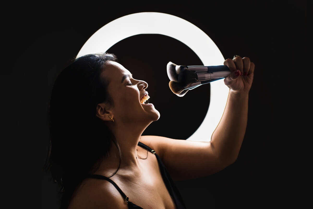 brand photo of a Make up Artist playing with brushes , ring light in her back