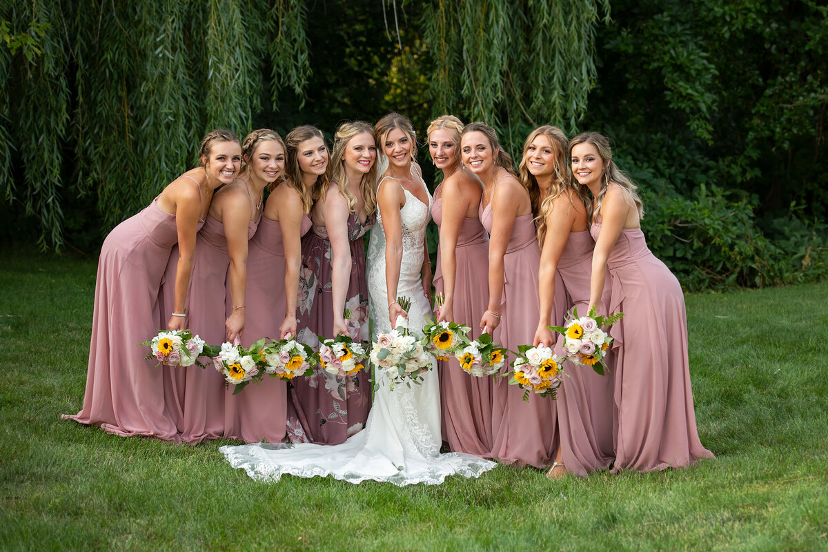 bride in white wedding dress  posing with 8 bridesmaids in pink dresses and flowers