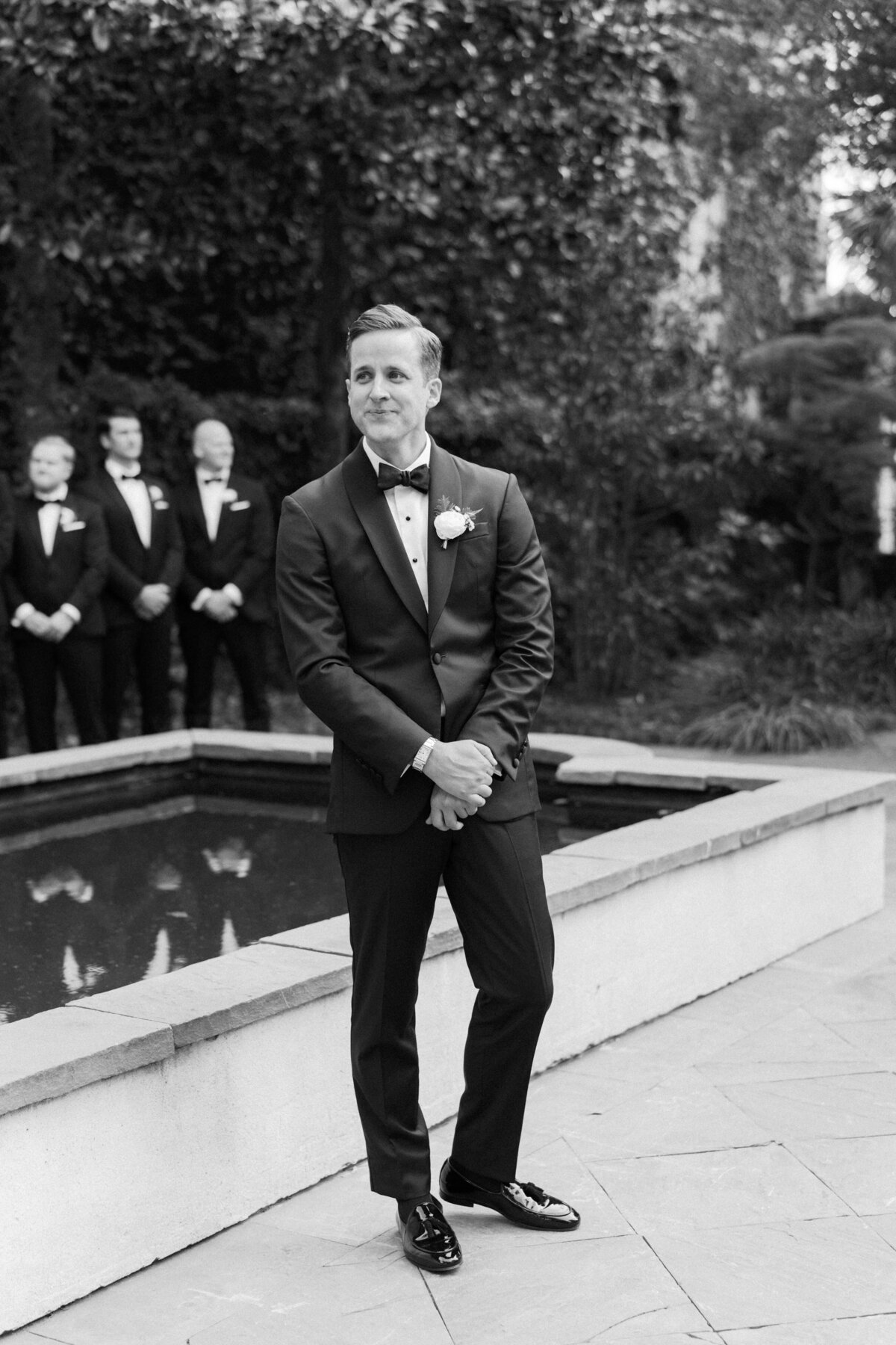 Black and white wedding ceremony photo of groom getting emotional seeing the bride walk down the aisle. Outdoor garden spring wedding ceremony in downtown Charleston. Kailee DiMeglio Photography.