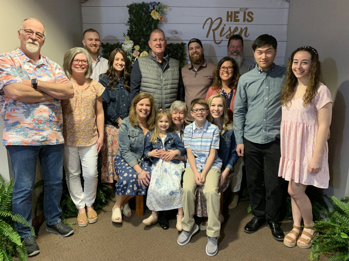 Family photo in front of "He is Risen" sign on Easter Sunday at Bartlett Chapel