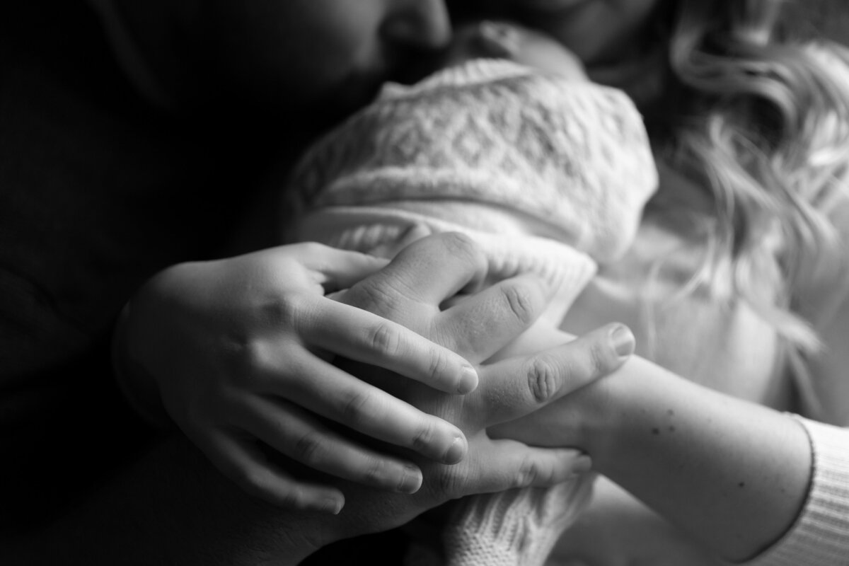 black and white close up of new parents holding hands while holding newborn baby to mother's chest