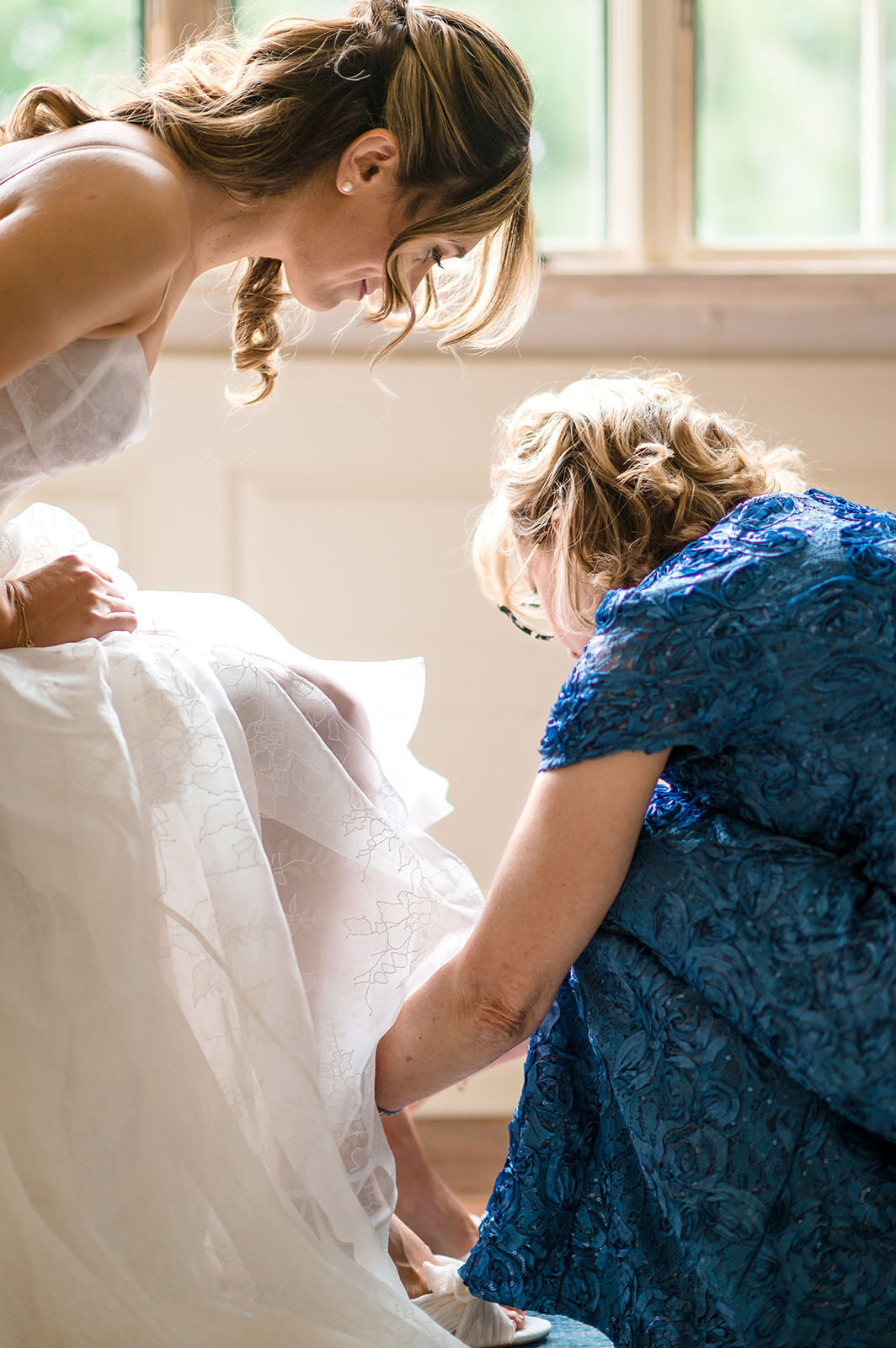 A woman helping a bride up on her shoes.