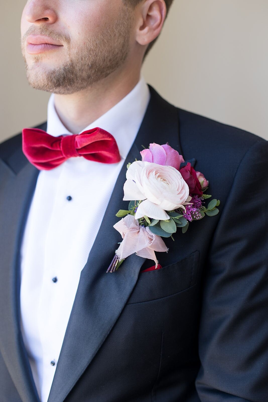 The groom has a full and bold boutonniere alongside his red velvet bowtie.