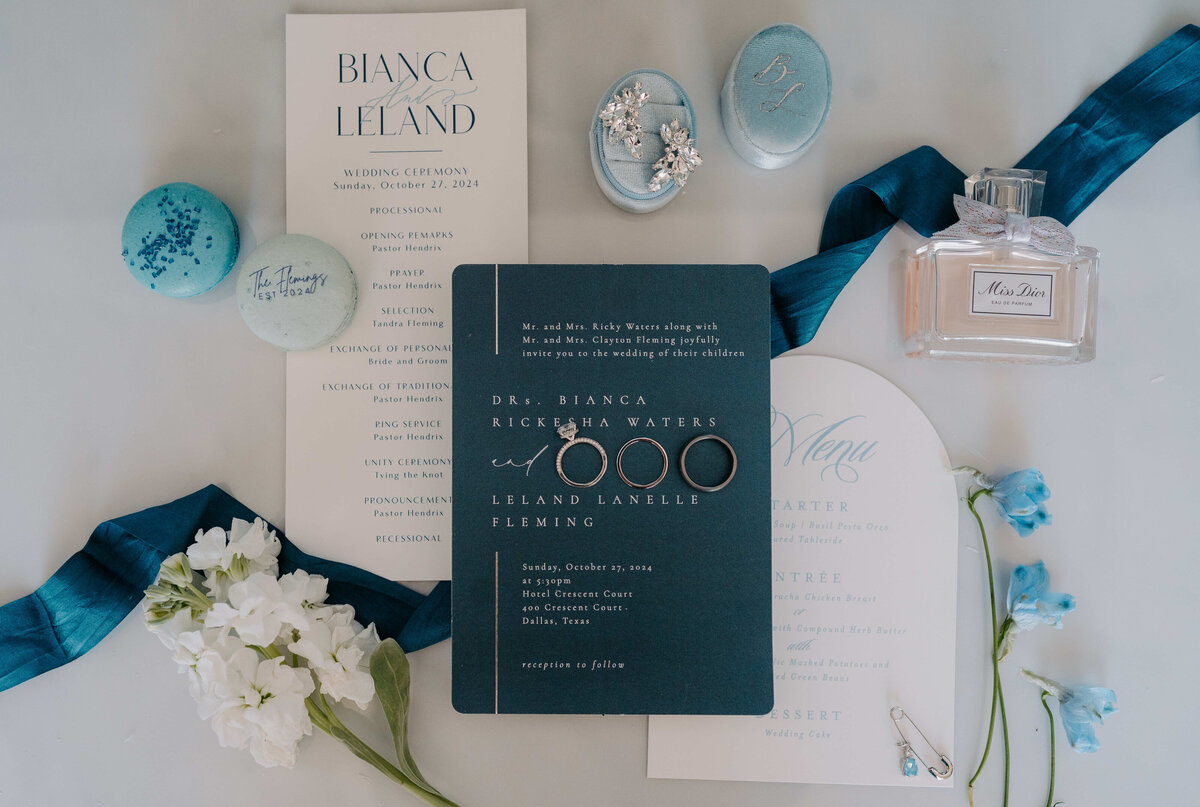 Elegant wedding invitation suite featuring blue and white tones, with rings, perfume, delicate floral accents, and ribbon, exuding a sophisticated charm.
