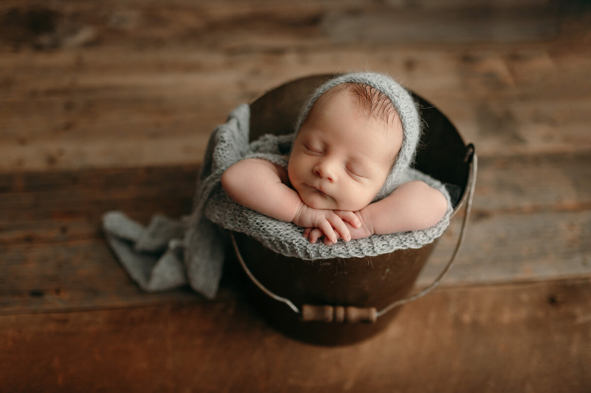 Sleeping baby boy poses, sleeping, for a portrait in our Waukesha, WI photo studio. Infant is wrapped in gray, woven blanket and wears a matching hat.