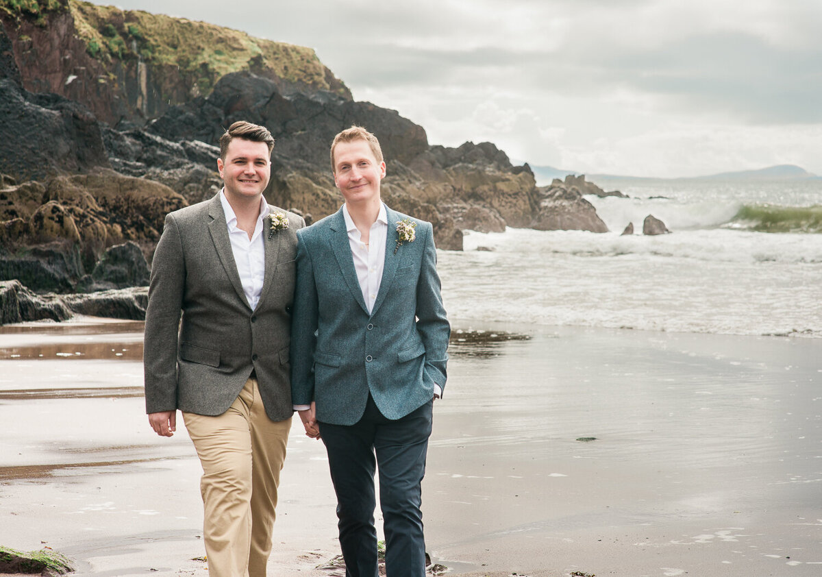 Two grooms in suits, walking on the beach together