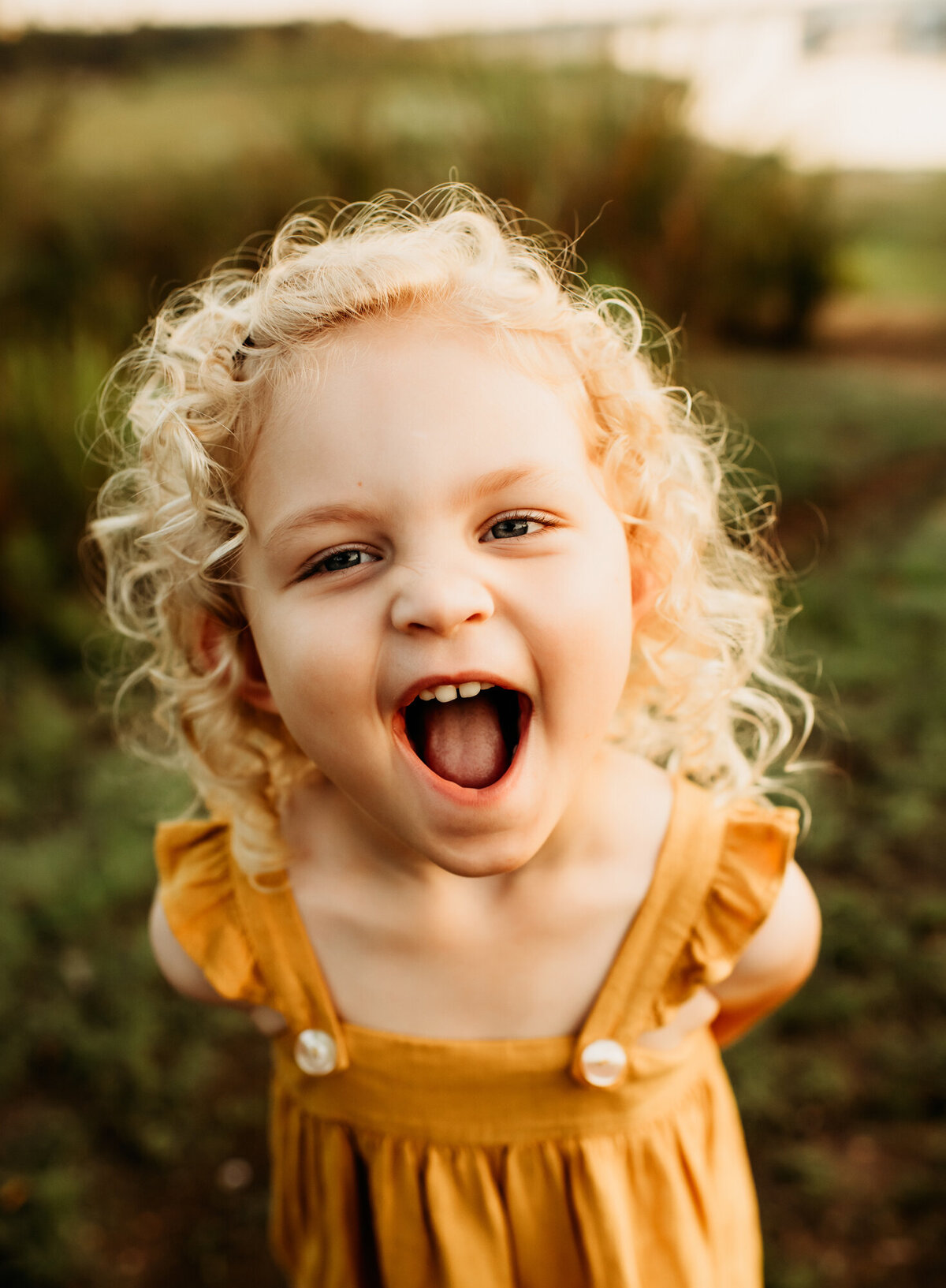 Little girl laughing at the camera in a yellow dress.