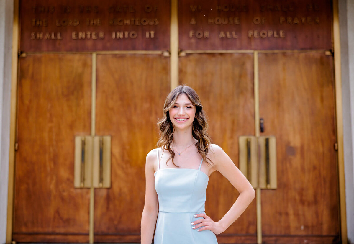 A teenage girl in a light blue dress stands with a hand on her hip for some Bellevue Bar and Bat Mitzvah Photography in front of a temple