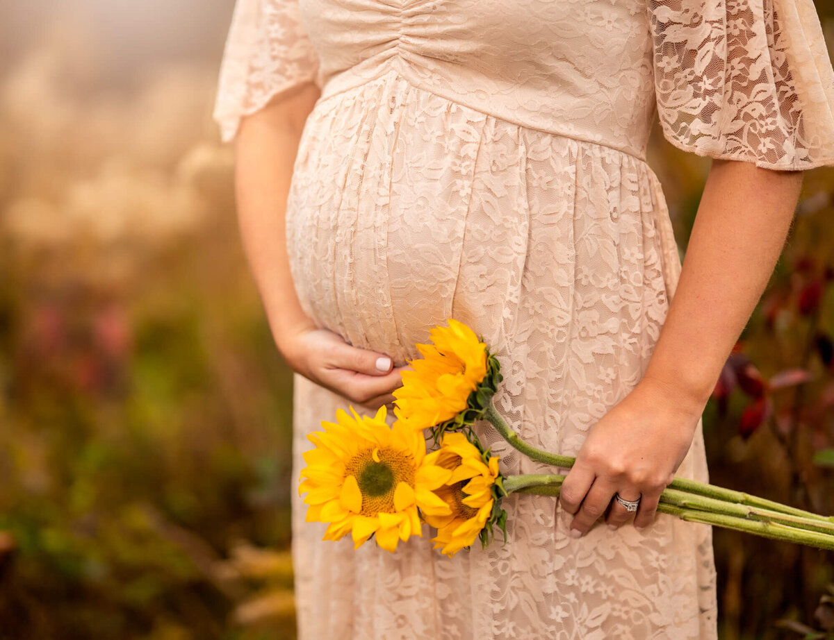 A mom cradles her baby bump while holding sunflowers in front of her belly