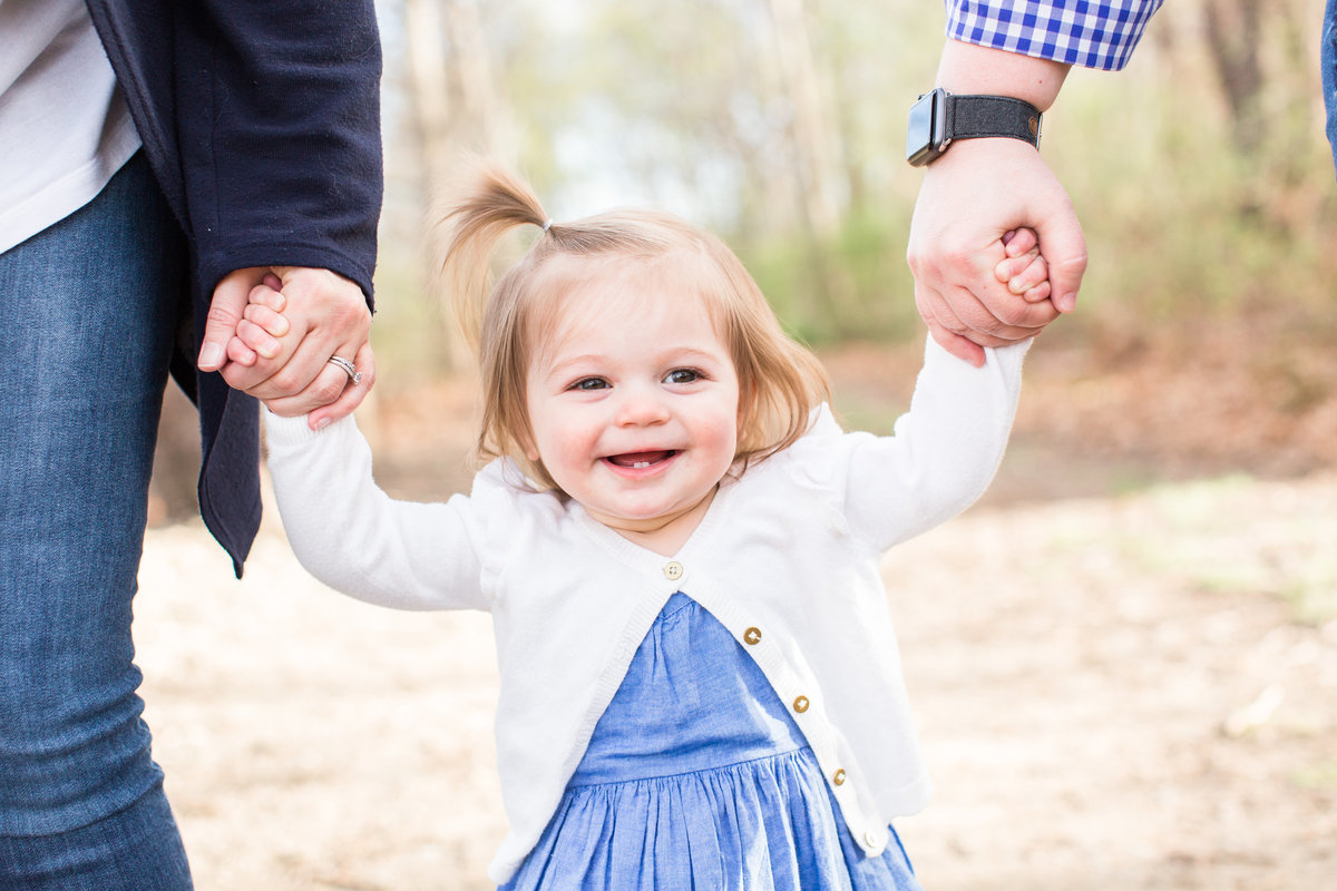 Little girl holding her parents' hands smiling at camera