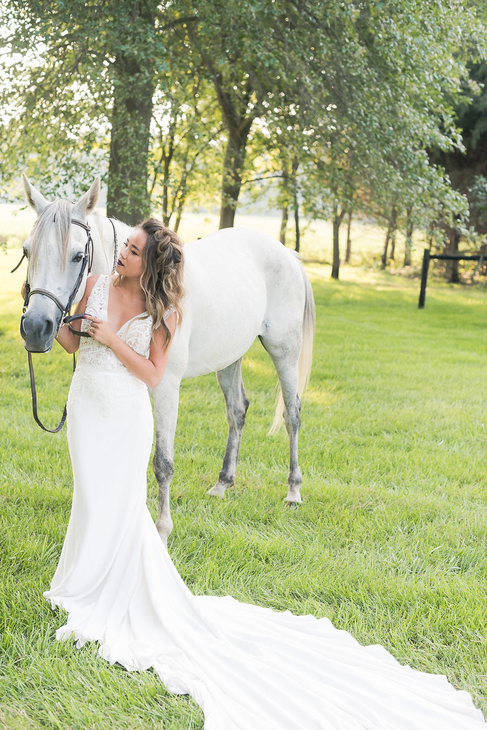 Wedding photographer capture of a woman in a white dress standing next to a white horse