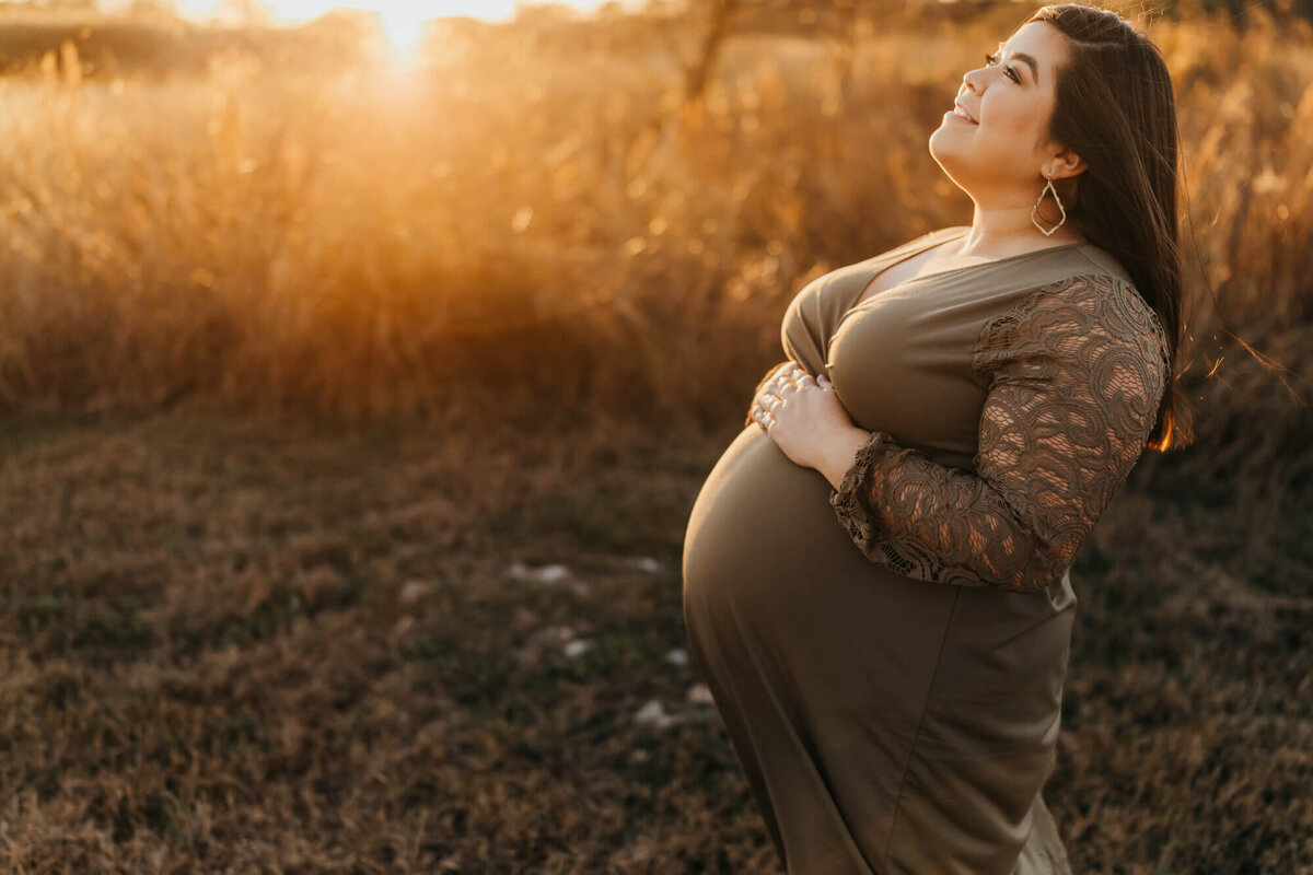 first time mama holds her belly wearing an olive dress in a field