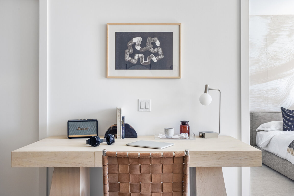 Modern home office with monumental thick light wood desk, woven leather chair and abstract black and white artwork