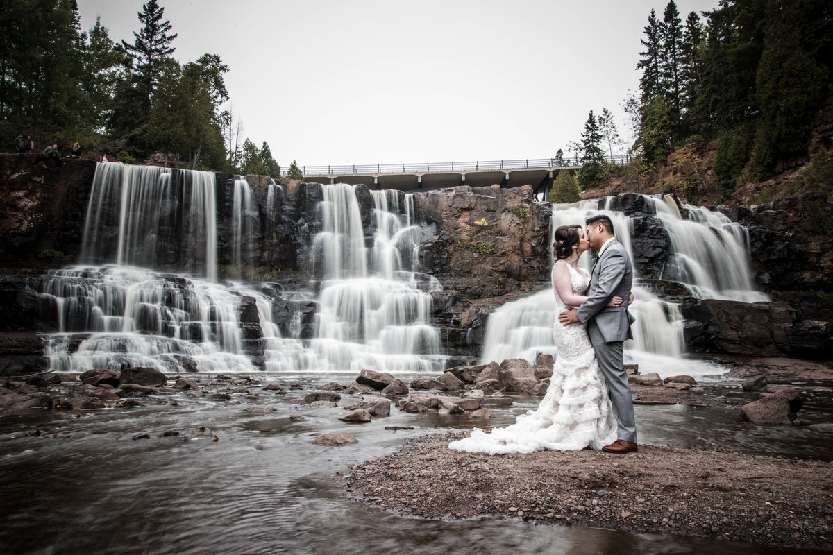 Bride and groom kiss in front of Gooseberry Falls in Minnesota.