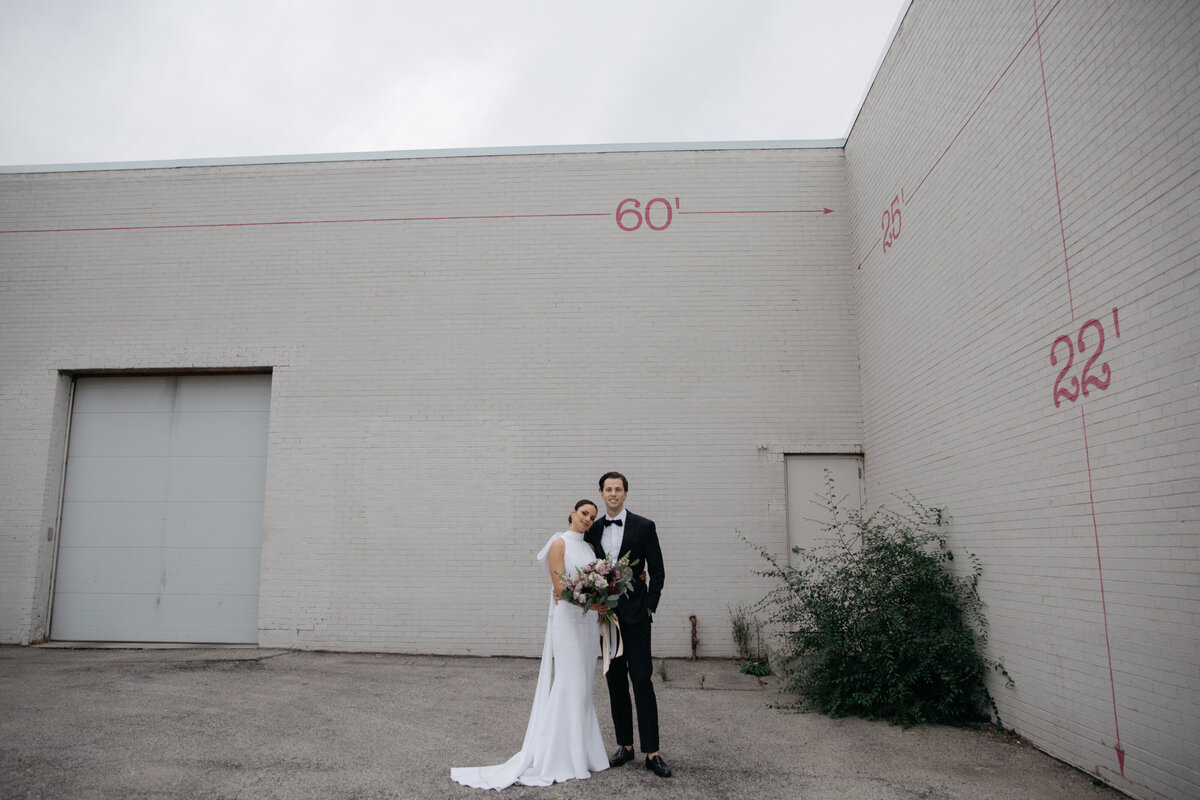 Wide angle full body view of bride and groom standing in front of brick industrial park in downtown Chicago