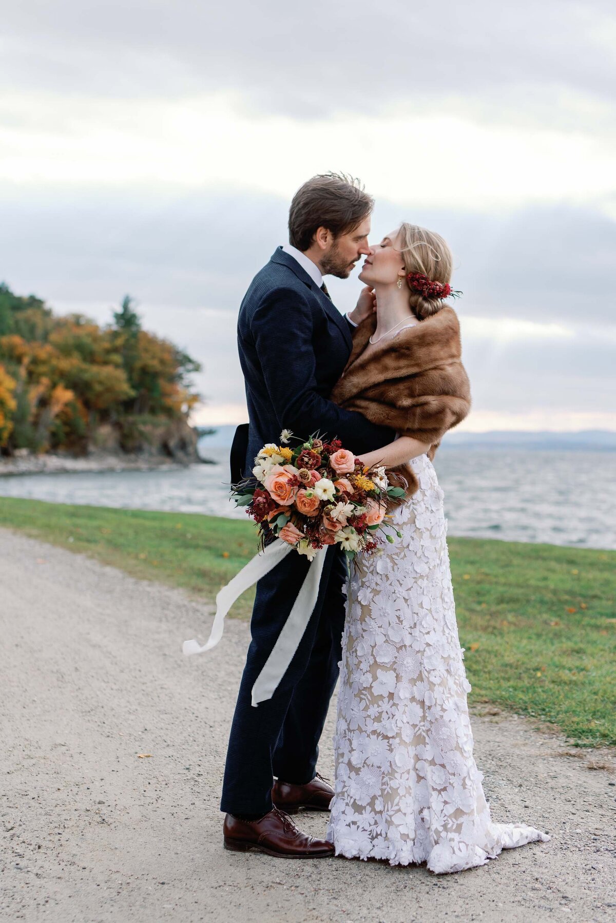 wedding couple kiss by shelburne farms lake with floral bouquet drifting in the wind