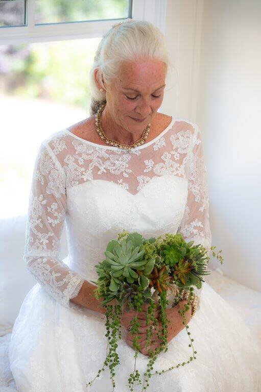 Elderly bride sits in wedding dress and looks down of bouquet of flowers, captured by wedding photographer sacramento, philippe studio pro.