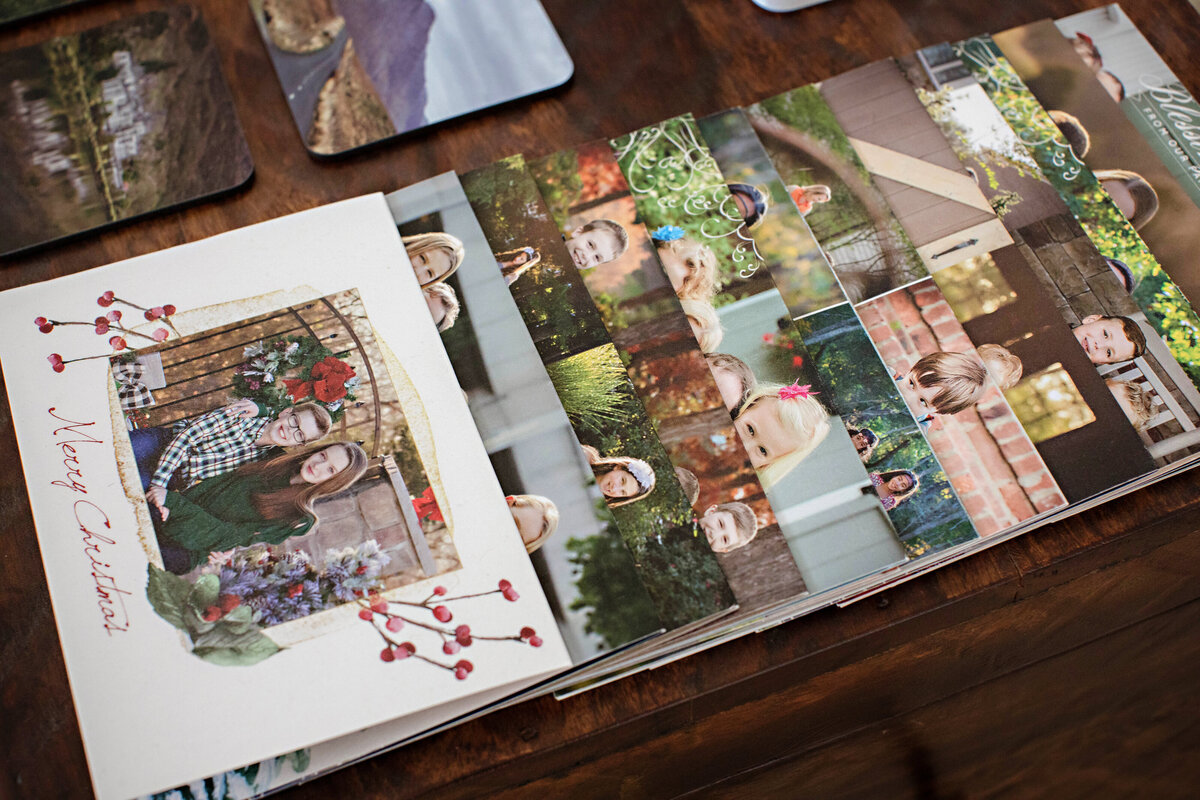 Custom press printed holiday card samples arranged in a line on a tabletop, showcasing a variety of seasonal designs, colors, and layouts for easy viewing and comparison.