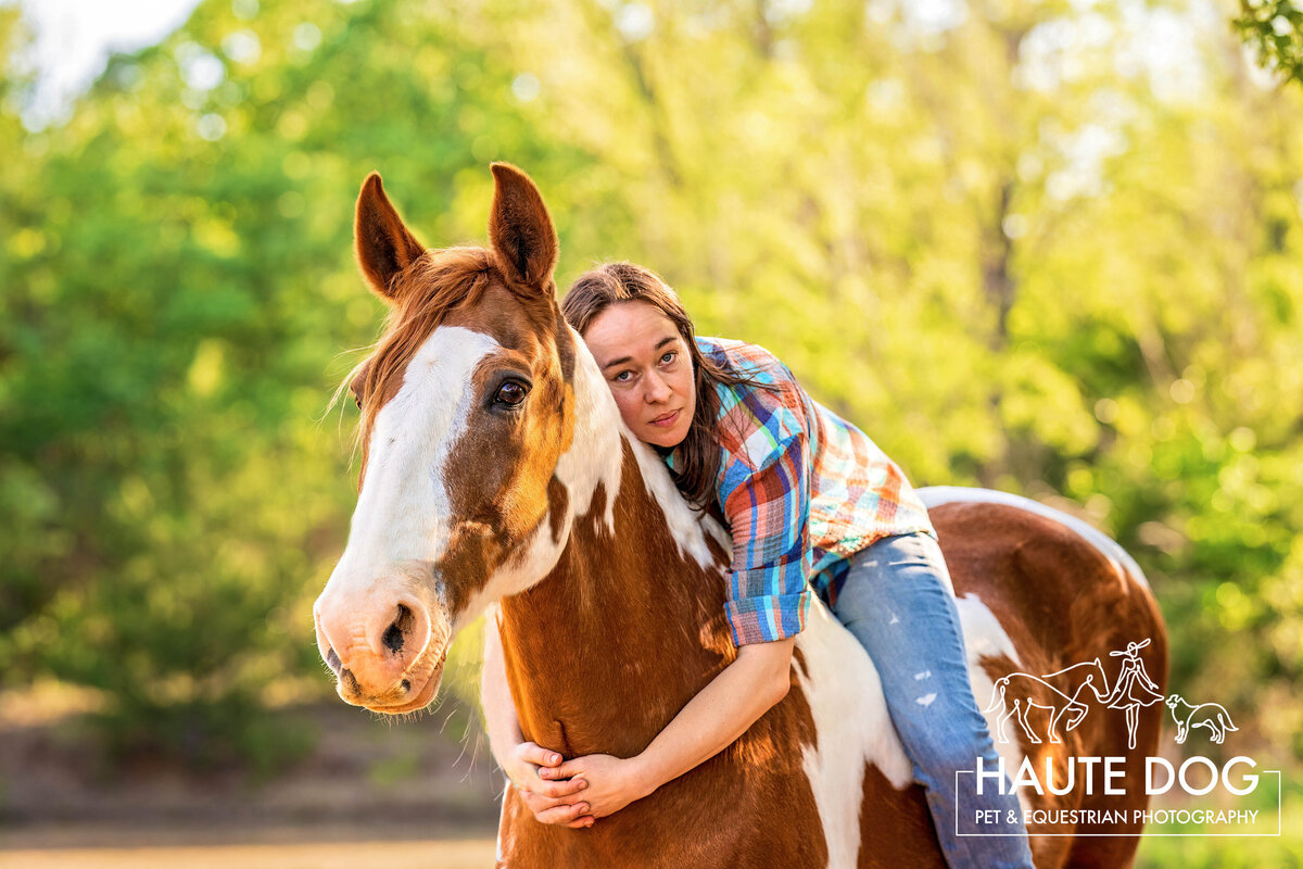 Equestrian wearing jeans and a plaid shirt sits on her paint Spotted Tennessee Walking Horse with her arms hugging his neck as they both look toward the camera.