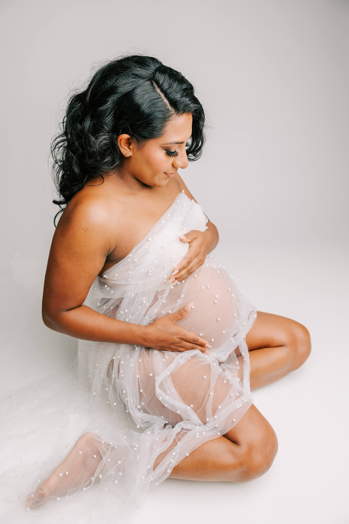 mom kneeling on ground with white fabric wrapped around her for maternity portrait