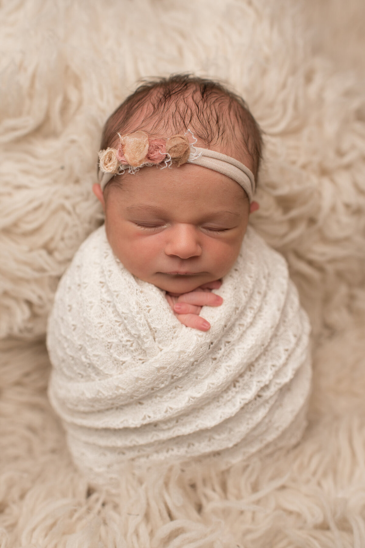 Newborn girl wrapped in white wrap in white fur