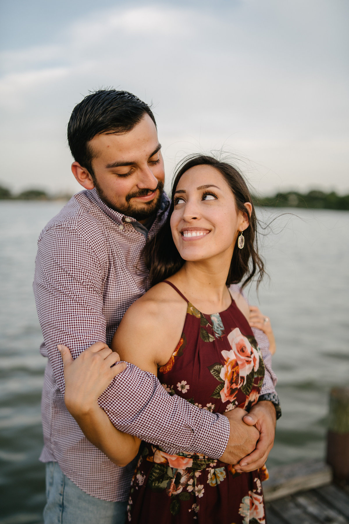 Fiancé is holding his bride to be on a wooden pier at Woodlawn Lake in San Antonio. They are engaged and soon to be married.