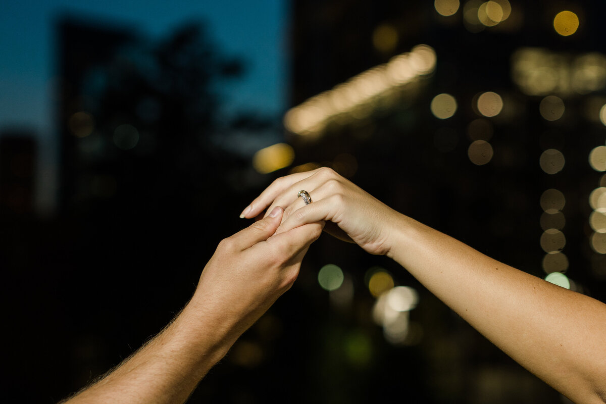 A detail shot of a couple's hands after popping the question during their proposal shoot in Dallas, Texas. The engagement ring can be clearly seen on the hand on the right while the out of focus Dallas skyline lights up the background.