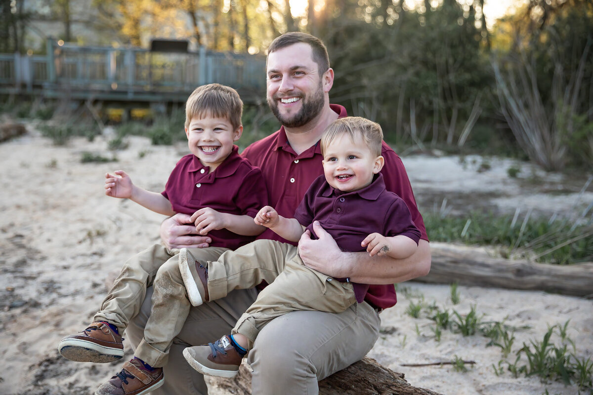 Dad sits with kids in his lap smiling during lifestyle family pictures in Harford County, Maryland