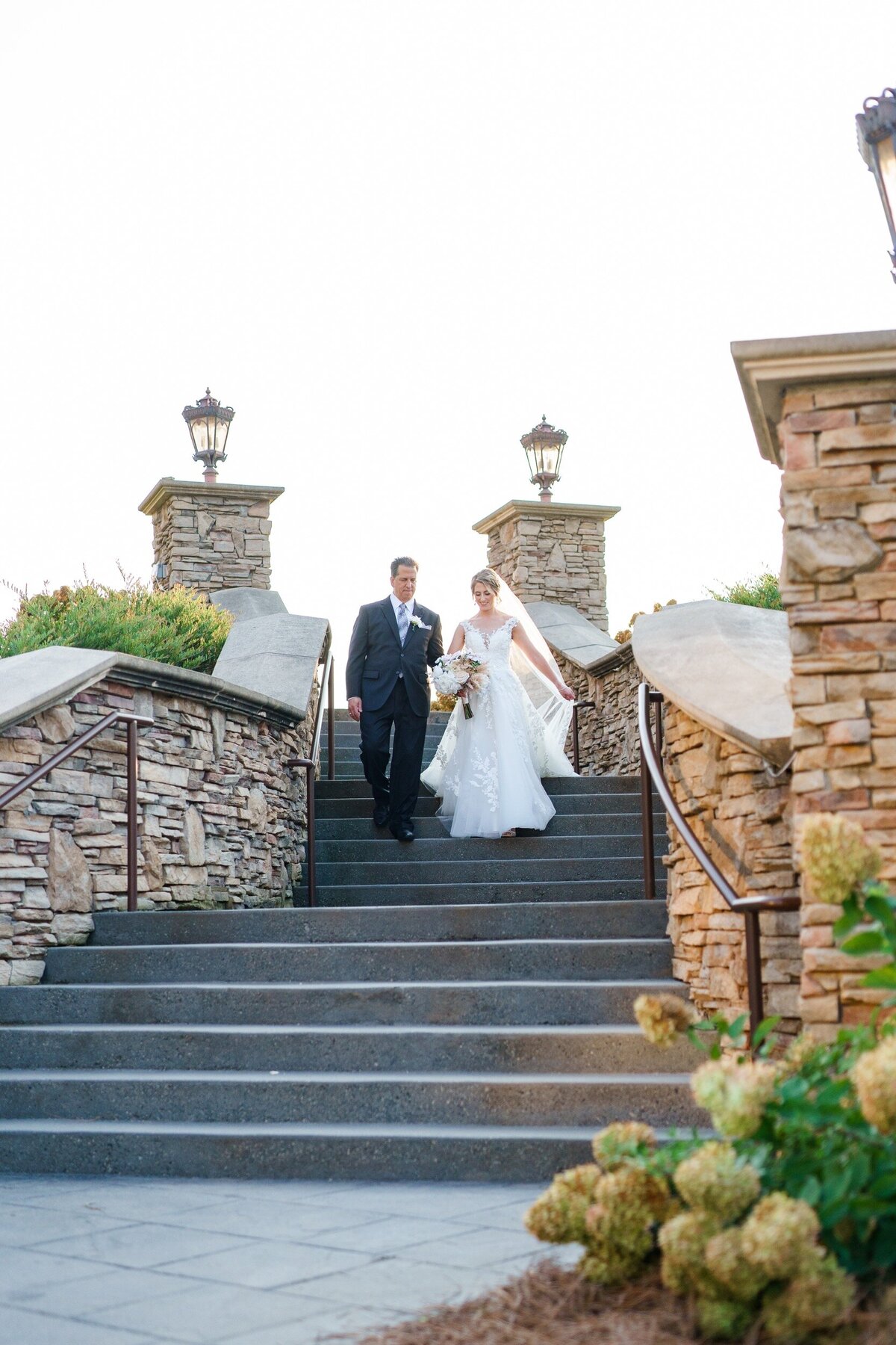 A father escorts his daughter down a stone staircase on their way to her wedding ceremony at a vineyard venue near Charlotte, NC.
