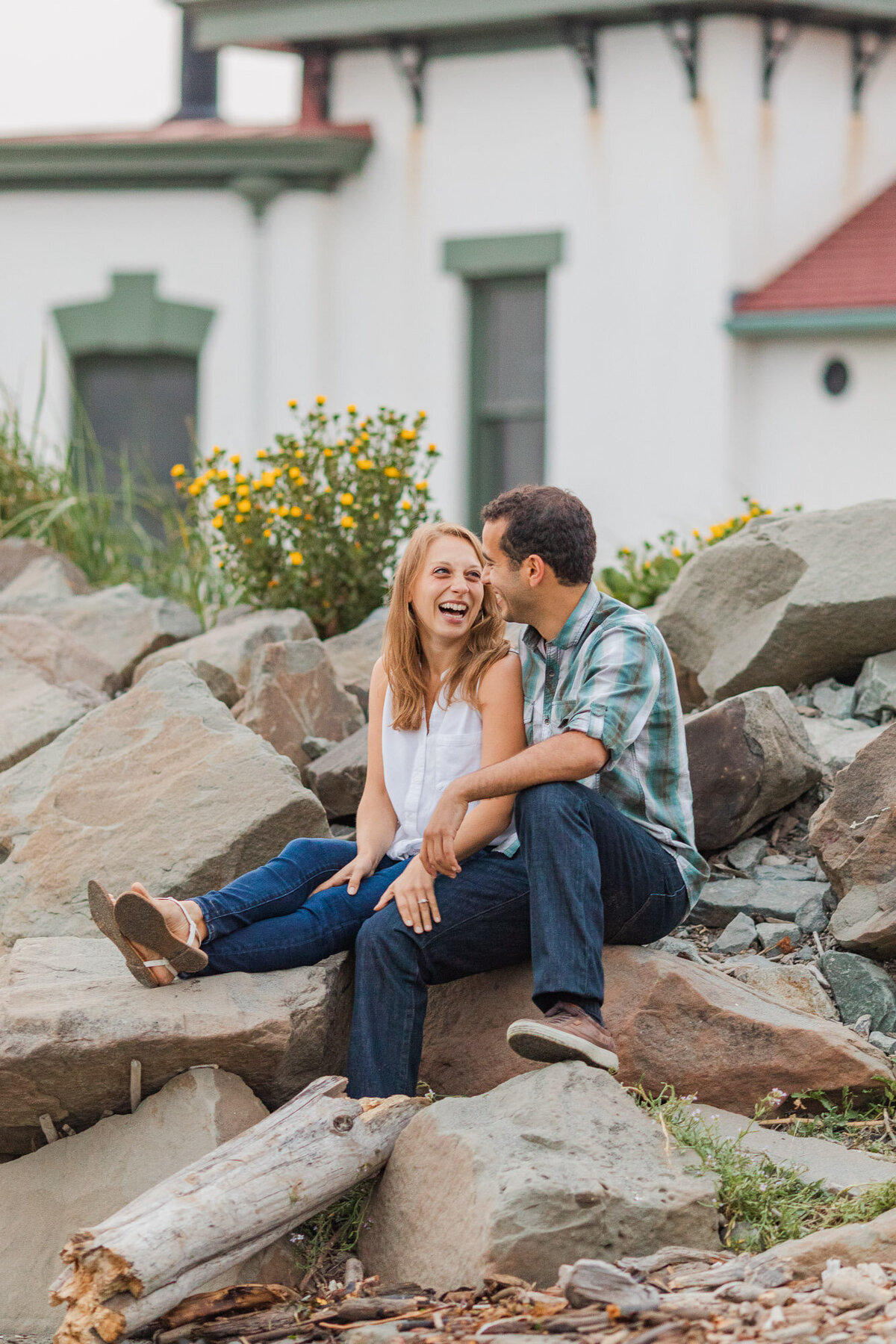 Happy PNW couple laugh at engagement session at lighthouse at Discovery Park in Seattle WA photo by Joanna Monger Photography