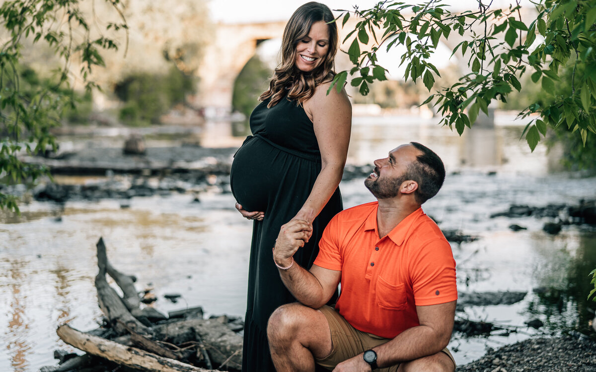 A pregnant woman and her partner gazing at each other with the iconic Stone Arch Bridge in Minneapolis in the background.