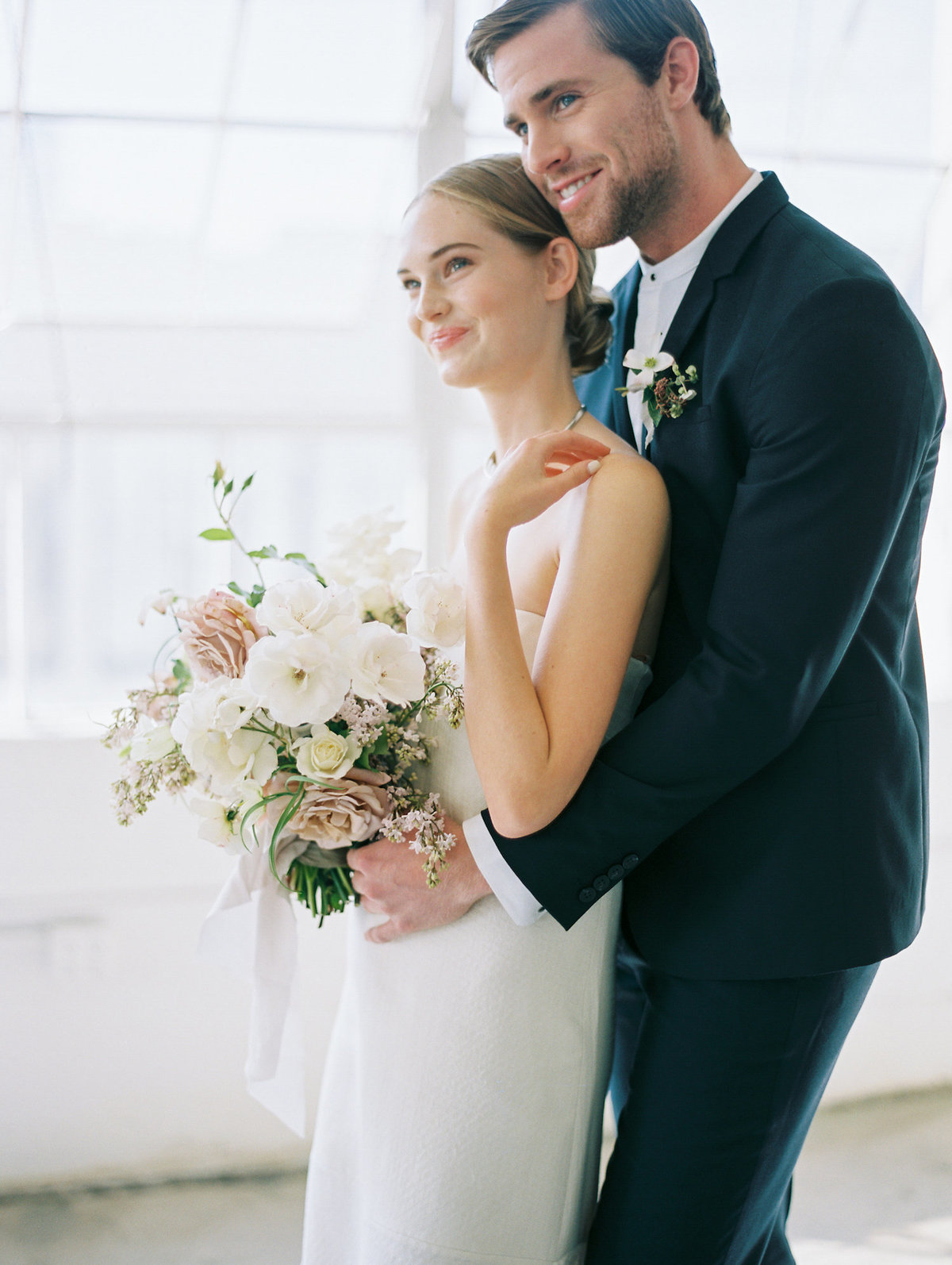 bride and groom hugging looking off camera with bouquet in hands