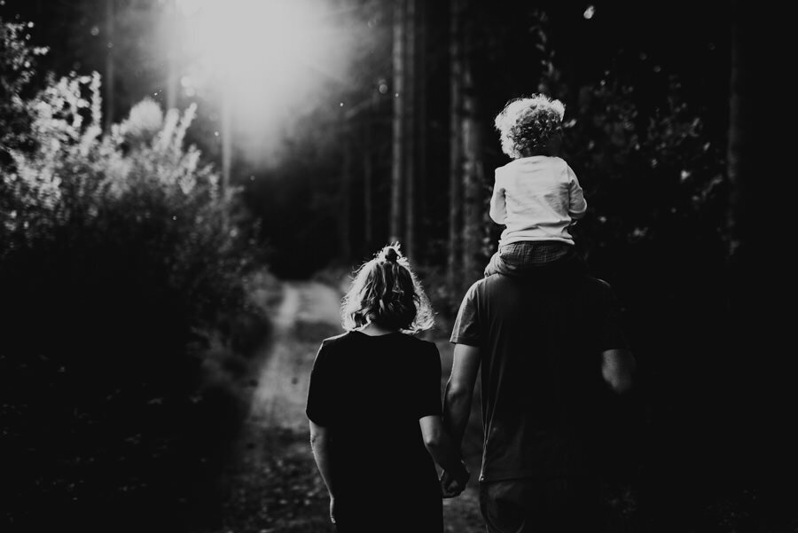 föräldrar håller hand och barnet sitter på pappas axlar under promenad i skogen