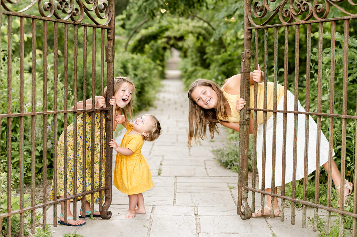 Sisters peeking around iron gate at a forest preserve family session near Naperville, IL.