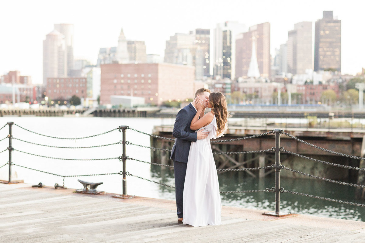 couple kissing in the Charlestown Navy Yard with Boston Skyline in the background
