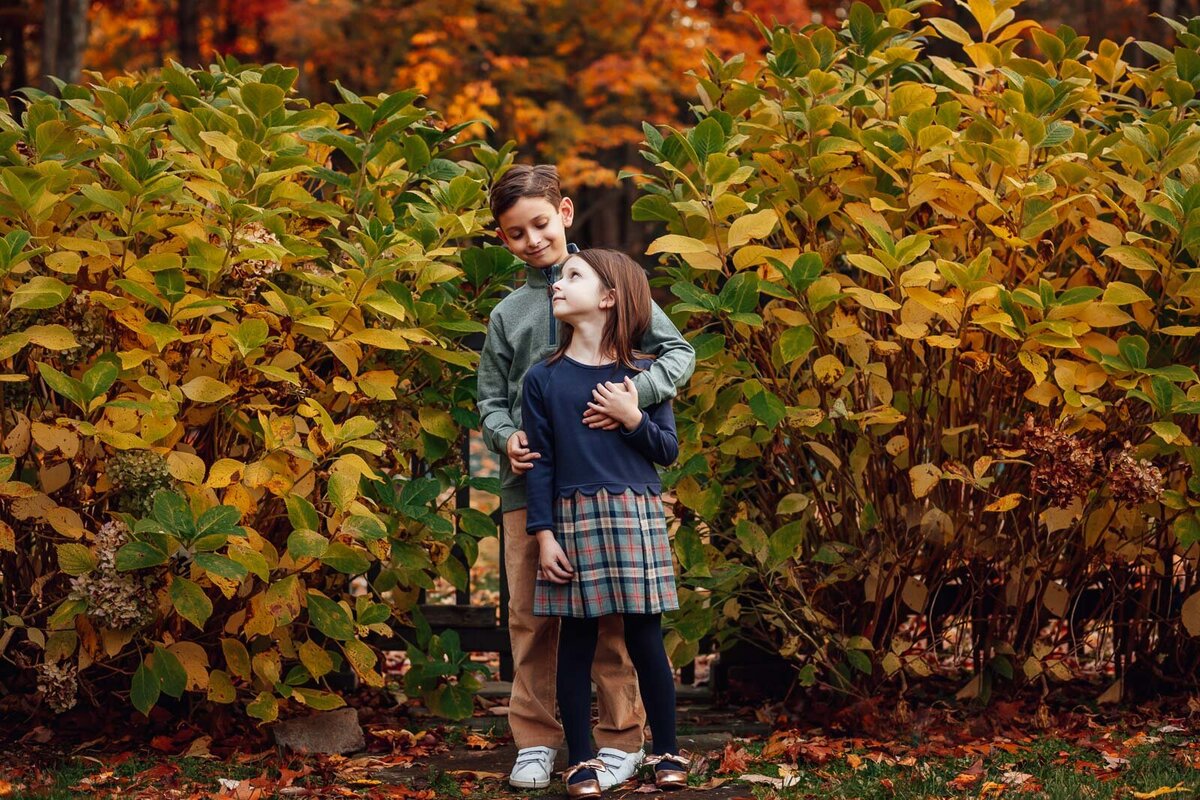 brother and sister in front of fall leaves during family photo session
