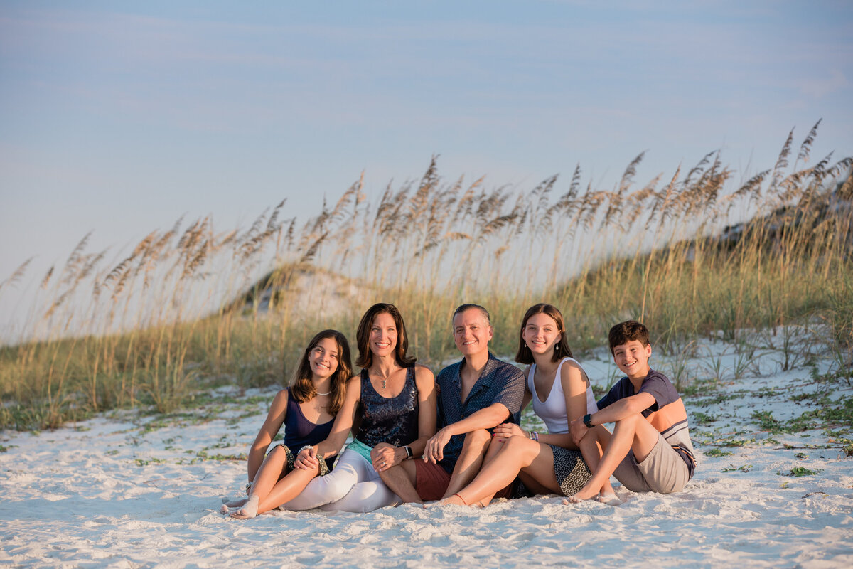 A family sitting in the sand with tall grass behind them