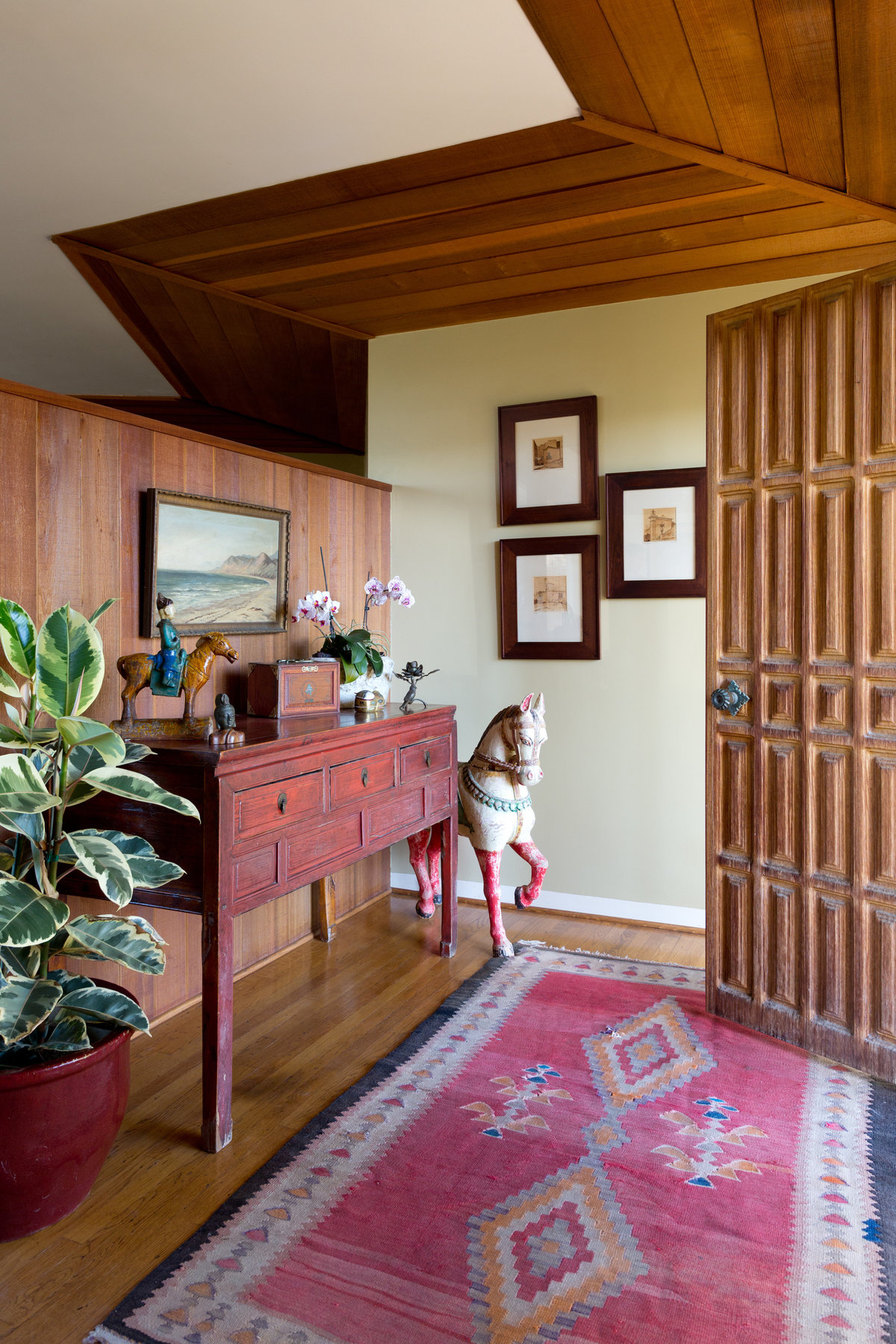 Entry with carved redwood door, vintage Navajo rug, red Chinese table, large wood horse, and rubber tree