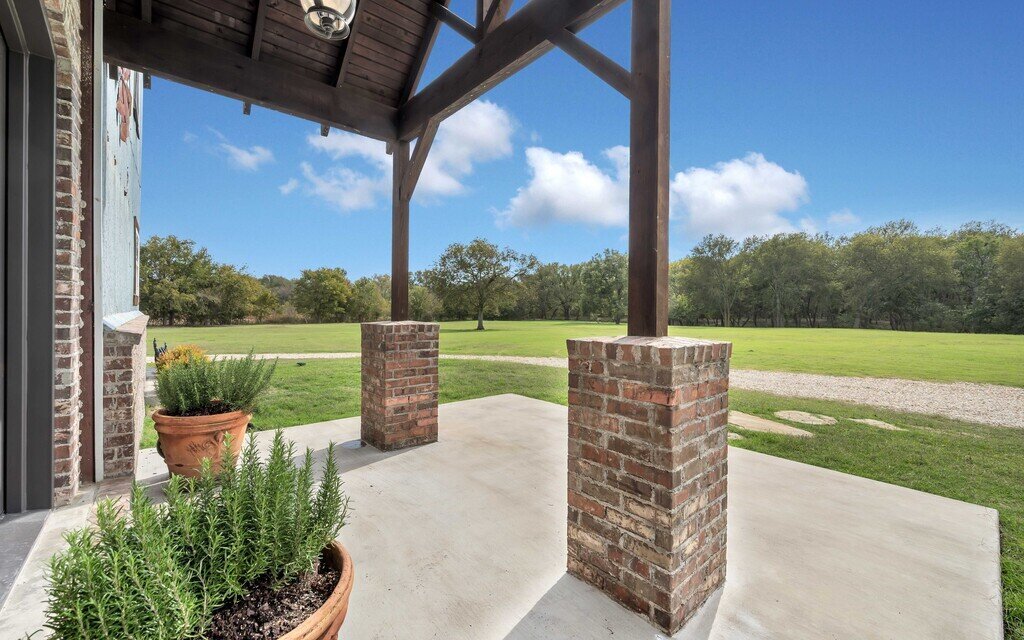 Front entrance covered porch with view of large front yard at this four-bedroom, four-bathroom vacation rental home and guest house with free WiFi, fully equipped kitchen, firepit and room for 10 in Waco, TX.