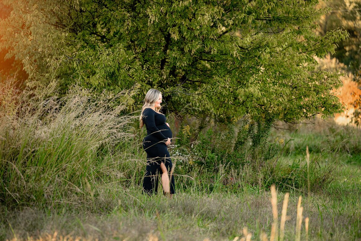 Charlotte Area expecting mom dressed in all black standing in a field looking off camera holding her belly