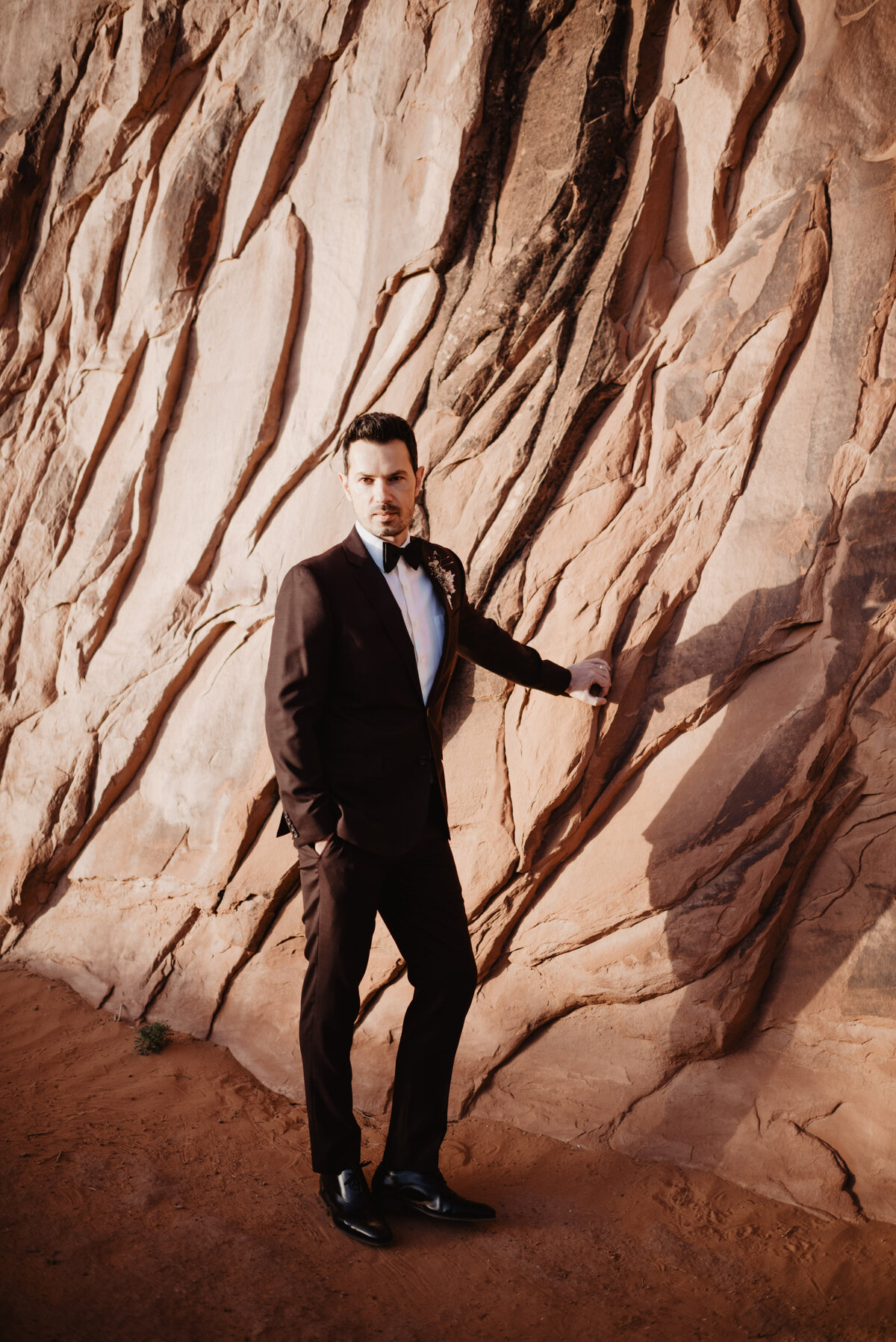 Utah elopement photographer captures groom touching red rock during groom portraits