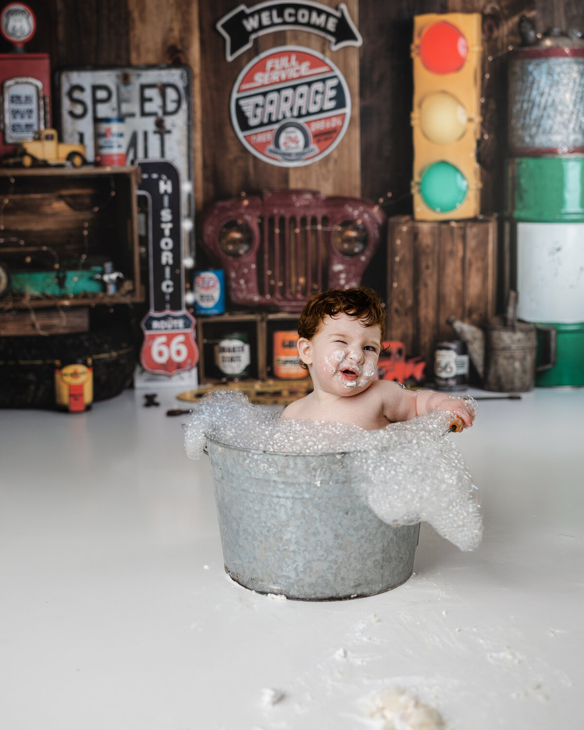One-year-old enjoying a bubbly soak in a tin tub after his garage-themed cake smash session. Photograph by Yucaipa cake smash photographer Kaitlyn Dawn Photography.