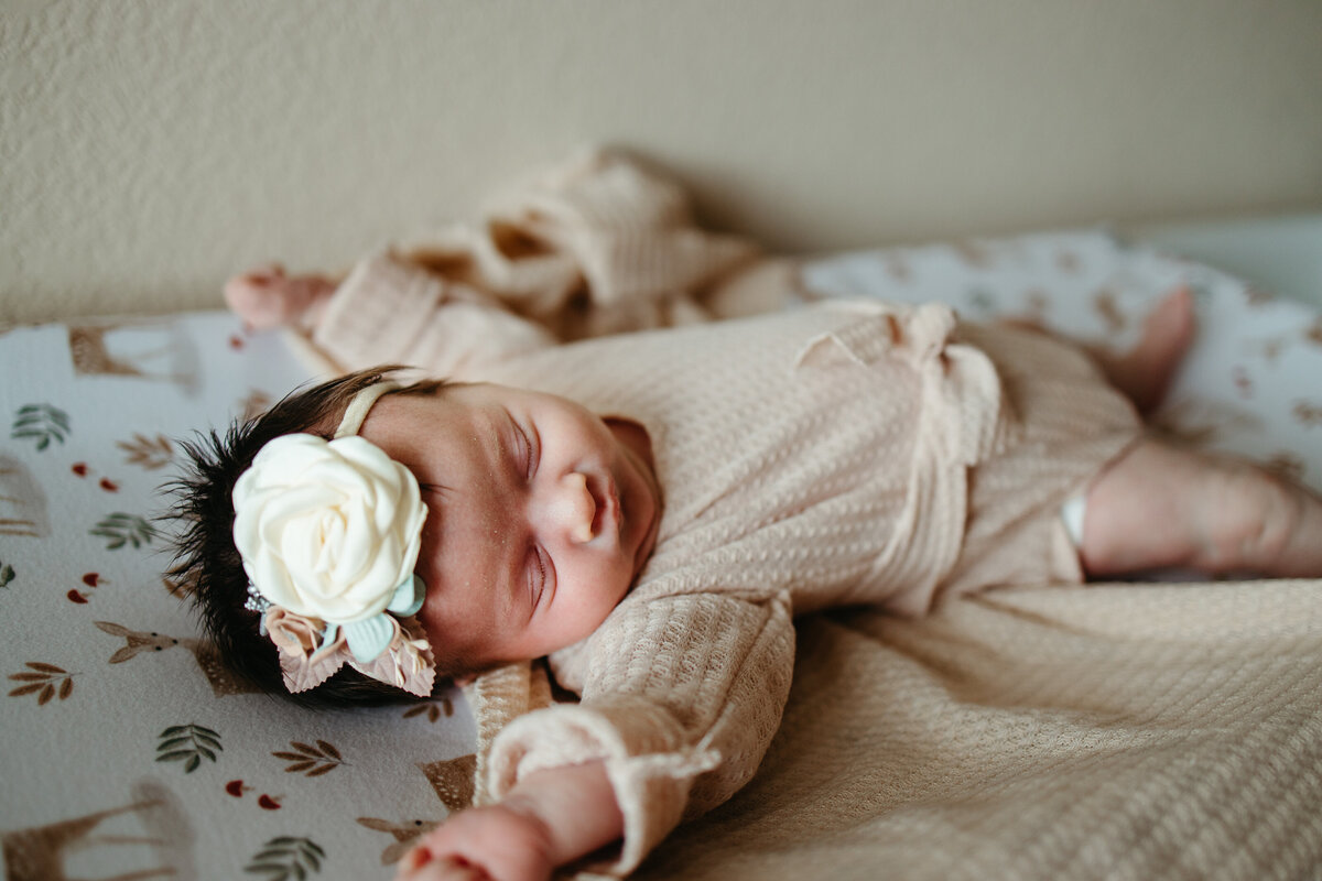 newborn baby girl stretches in nursery in a tan sleeper and white bow