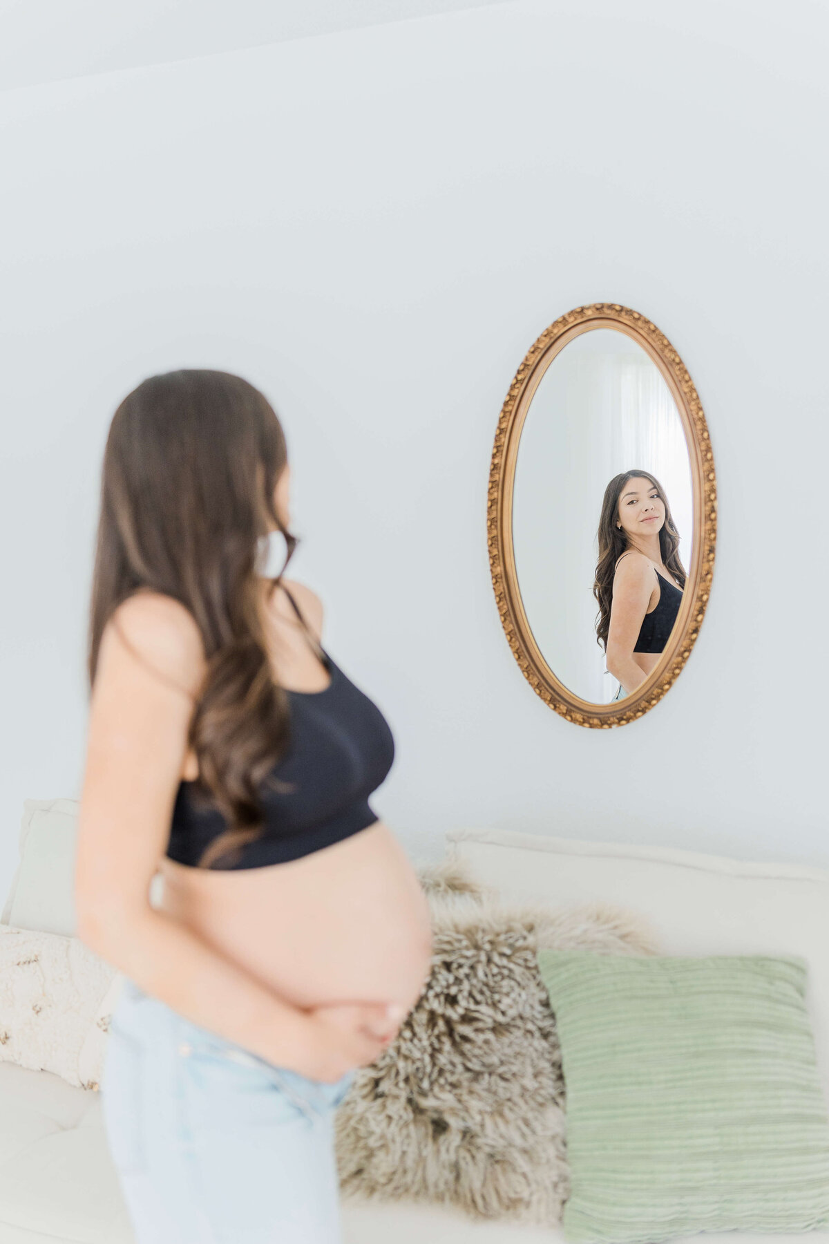Pregnant mother standing while looking at pregnant self in the mirror reflection