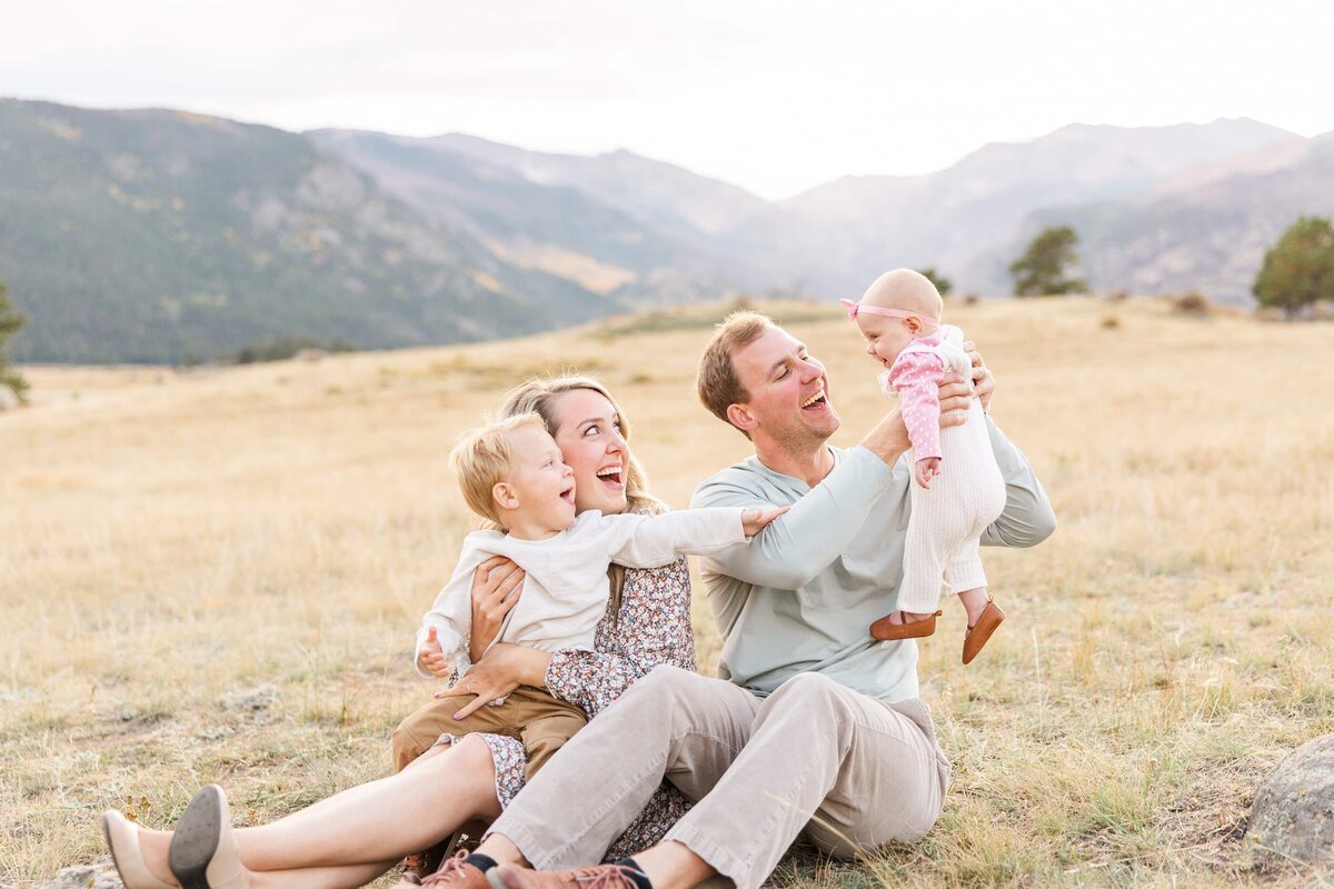 family sitting on the grass  smiling at baby girl in Rocky Mountain National Park