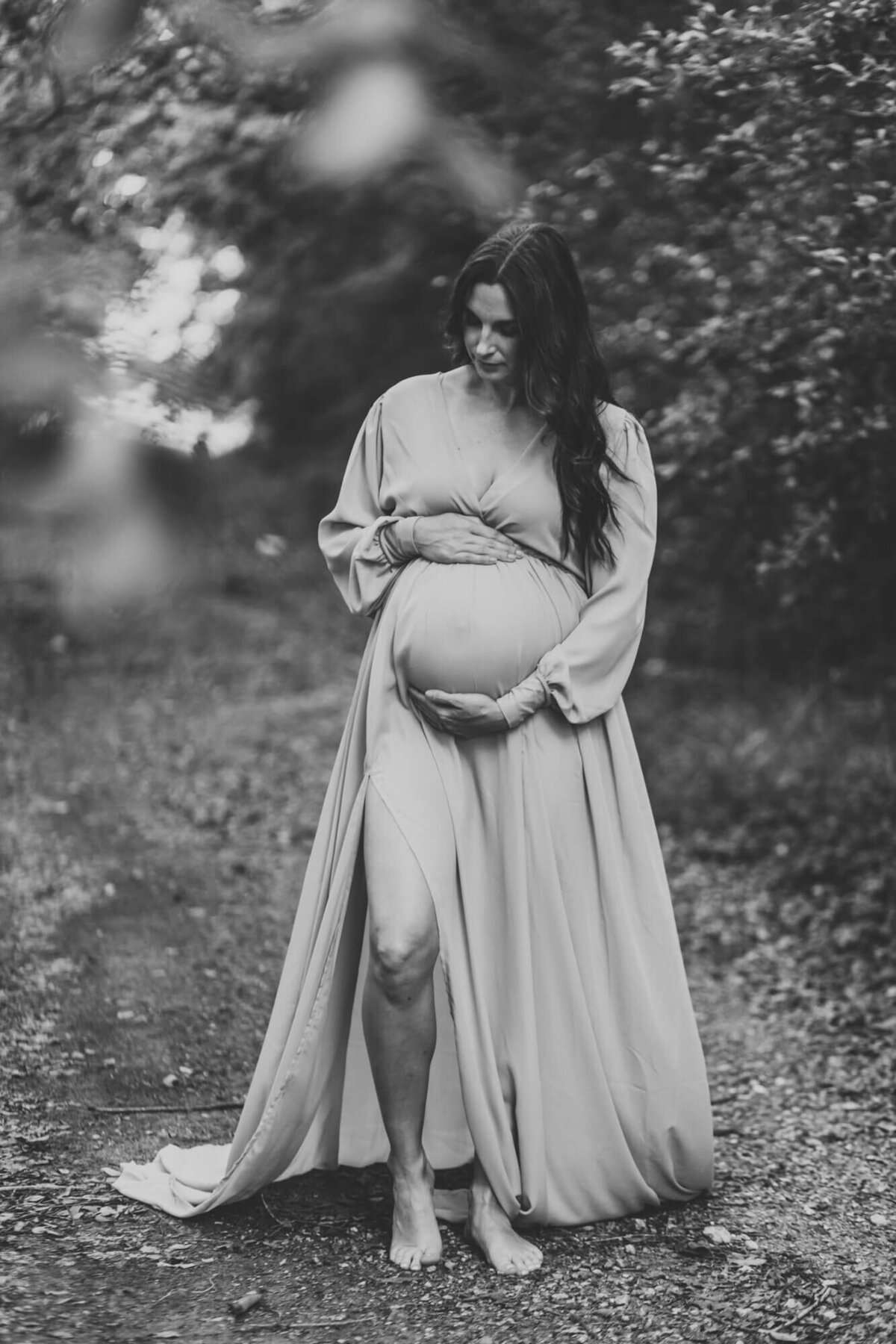 black and white image of mother standing in woods holding her belly.